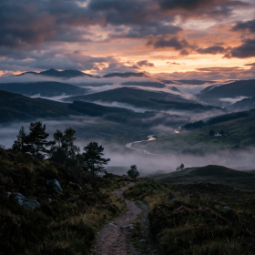 Winding river in misty valley with hills and trees at sunset